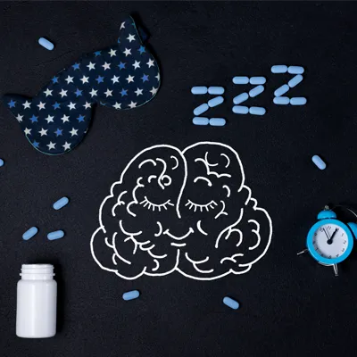 Illustration of a sleeping brain with sleep mask, alarm clock and blue capsules forming “ZZZ” on a dark background