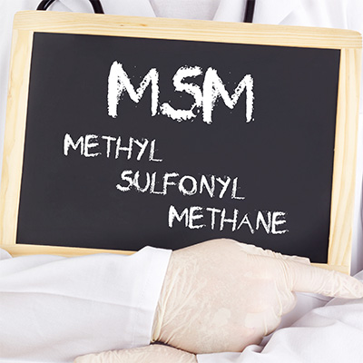 Tafel mit Aufschrift „MSM Methyl Sulfonyl Methane“ vor Person im Laborkittel – sachliche Darstellung