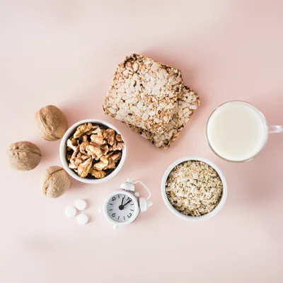 Walnüsse, Haferflocken, Knäckebrot und Milch neben einem Wecker auf rosafarbenem Hintergrund – Ernährung und Schlaf