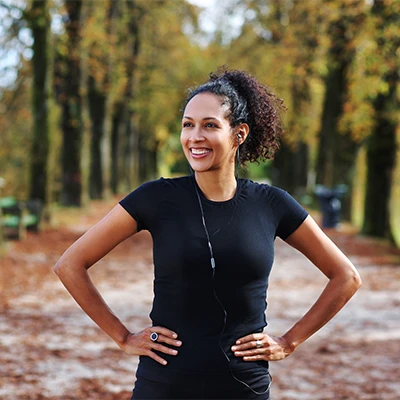 Smiling woman in black sportswear standing on forest path – warm daylight, active atmosphere