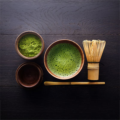 Matcha set with tea bowl, matcha powder, bamboo whisk and spoon on a dark wooden table